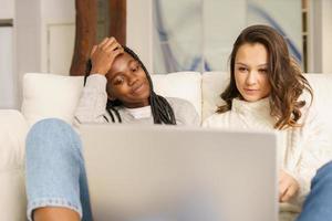 duas amigas estudante sentadas no sofá em casa usando um laptop. foto