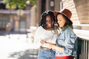 dois amigos olhando para o smartphone juntos. mulheres multiétnicas. foto