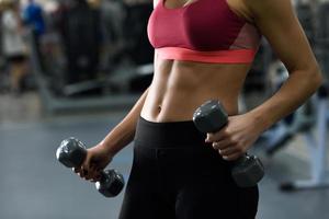 jovem com abdômen lindo levantando halteres na academia foto