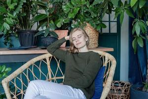 jovem loira sentada em uma cadeira confortável rodeada de plantas foto