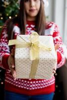 jovem de suéter vermelho segurando uma pilha de presentes de natal foto