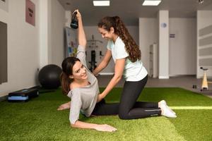 Fisioterapeuta ajudando jovem mulher caucasiana com exercícios com halteres foto