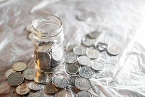 vidro jarra com espalhados moedas em reflexivo superfície foto