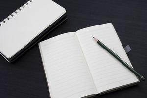 mesa preta com caderno e lápis em cima. uma maquete de notebook na mesa como um layout de área de trabalho. objeto de escritório isolado em fundo preto. foto