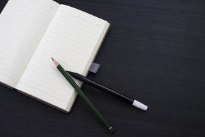 mesa preta com caderno e lápis em cima. uma maquete de notebook na mesa como um layout de área de trabalho. objeto de escritório isolado em fundo preto. foto