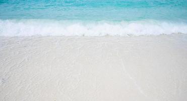 praia com areia branca e ondas do oceano azul suave foto