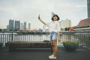 adolescente asiático tirando foto por telefone inteligente, parado na rua da cidade