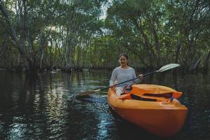 jovem asiática navegando de caiaque no rio manguezal foto