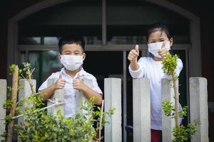 crianças asiáticas usando máscara de proteção em pé dentro da cerca da casa