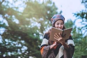 mulher asiática viajar natureza. viajar relaxar. estudo ler um livro. educação na natureza escreva uma nota em um parque público no verão. Na Tailândia foto