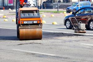 pequenos equipamentos rodoviários, um rolo-compactador vibratório e um compactador trabalham para reparar a faixa de rodagem. foto