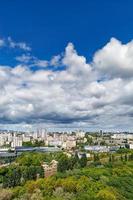 uma paisagem urbana com um parque verde, áreas residenciais e uma torre de tv contra um céu azul brilhante com nuvens espessas.