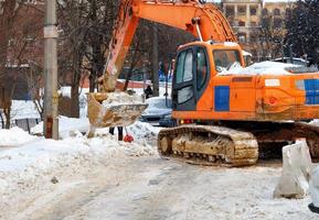 uma grande escavadeira com uma caçamba de metal limpa a faixa de rodagem de uma rua da cidade de uma abundância de neve compactada. foto
