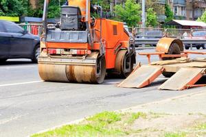 O rolo-compactador vibratório pesado é descarregado de um trailer de plataforma baixa e fica na estrada. foto