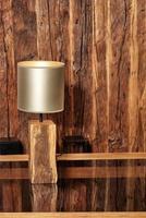 elegante lâmpada de leitura e uma velha parede de madeira rachada refletem em uma superfície de madeira polida. foto