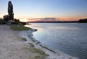 em uma praia fluvial, um pôr do sol brilhante de verão e um reflexo dos raios de sol nas águas calmas do rio foto