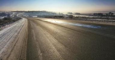 uma velha estrada de asfalto é iluminada pelo sol na manhã de inverno. foto