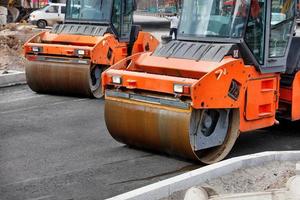 dois grandes rolos compactadores vibratórios compactam o asfalto fresco em um novo trecho de estrada. foto