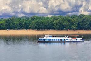 um bonde fluvial corre ao longo das margens do dnipro tendo como pano de fundo uma praia deserta em antecipação a uma tempestade iminente. foto