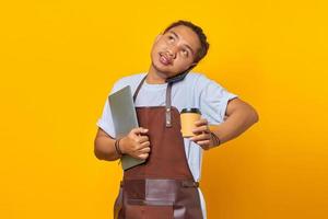 retrato de homem asiático bonito ocupado atendendo chamadas. ambas as mãos carregando um laptop e uma xícara de café foto