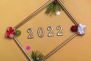 layout de ano novo em um fundo bege bolas de natal, galhos de uma árvore de natal, uma caixa de presente e uma moldura dourada, uma maquete de um cartão postal, um convite foto