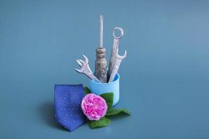 vaso criativo com chave de fenda de ferramentas. sobre um fundo colorido uma rosa rosa uma gravata azul e um vaso com ferramentas. minimalismo para o dia dos pais. close up, monochrome.still life foto