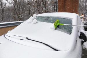 escovando a neve com uma escova longa do para-brisa do seu carro foto