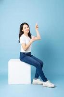 retrato de menina asiática sentada em um cubo branco, isolado em um fundo azul foto