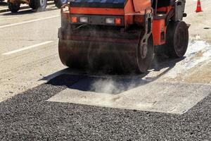 um rolo compactador vibratório pesado compacta asfalto na estrada a ser reparada. foto