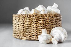 cogumelos champignon em uma cesta de vime redonda sobre uma mesa de madeira branca foto