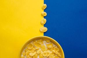 flocos de milho com leite na tigela amarela sobre fundo azul e amarelo foto