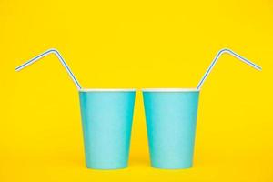dois copos de papel azuis com canudos de plástico coloridos bebendo em fundo amarelo foto