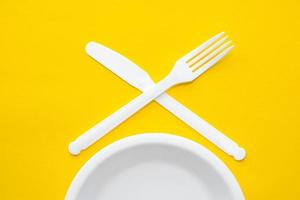 garfo, faca e prato de plástico branco sobre fundo amarelo foto