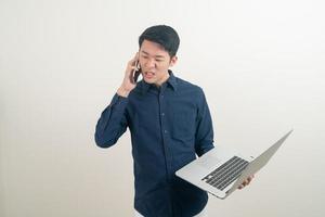 homem asiático falando em smartphone ou celular e segurando uma mão no laptop foto