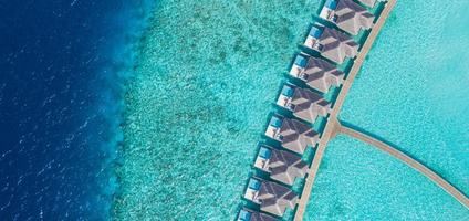 vista aérea da ilha das Maldivas, resort de villas de luxo na água e cais de madeira. céu deslumbrante e praia da lagoa do oceano. férias de verão férias e conceito de viagens. panorama da paisagem aérea do paraíso foto