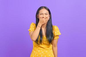 retrato de uma jovem asiática rindo cobrindo a boca com a mão no fundo roxo foto