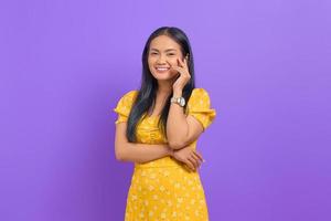 jovem asiática sorridente usando um vestido amarelo e parecendo confiante em um fundo roxo foto