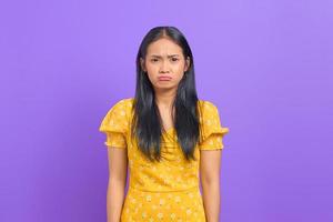 retrato de uma jovem asiática chateada com um vestido amarelo sobre fundo roxo foto