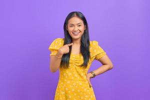 retrato de uma jovem mulher asiática sorridente, apontando para si mesma com orgulho em fundo roxo foto