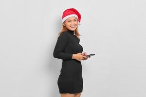 retrato de uma jovem asiática sorridente com chapéu de Papai Noel, usando telefone celular isolado sobre fundo branco foto