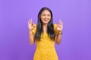 jovem asiática alegre faz um gesto de aprovação, demonstra símbolo de aprovação em fundo roxo