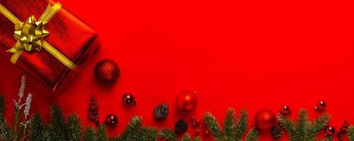 fundo de Natal com galhos de pinheiro, presente ou presente e bola vermelha no fundo da bandeira vermelha. vista de cima com espaço de cópia