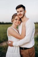 garota com um vestido de verão branco e um cara com uma camisa branca em uma caminhada ao pôr do sol com um buquê foto