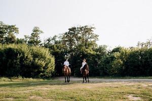 uma garota com um vestido de verão branco e um cara com uma camisa branca em uma caminhada com cavalos marrons foto