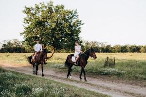 uma garota com um vestido de verão branco e um cara com uma camisa branca em uma caminhada com cavalos marrons foto