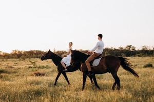 uma garota com um vestido de verão branco e um cara com uma camisa branca em uma caminhada com cavalos marrons foto