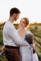 garota com um vestido de verão branco e um cara com uma camisa branca em uma caminhada ao pôr do sol com um buquê foto