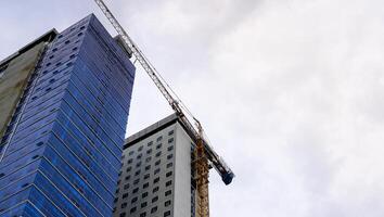 o canteiro de obras com um guindaste na frente dos edifícios arranha-céus. um prédio alto com vidros nas paredes está em construção. foto