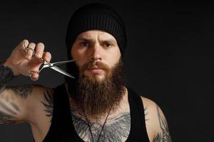 retrato de um homem corajoso com uma barba, ele segura uma tesoura perto de sua barba e olha para a câmera foto