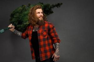 homem bonito com cabelo comprido segurando uma árvore de natal sintética foto